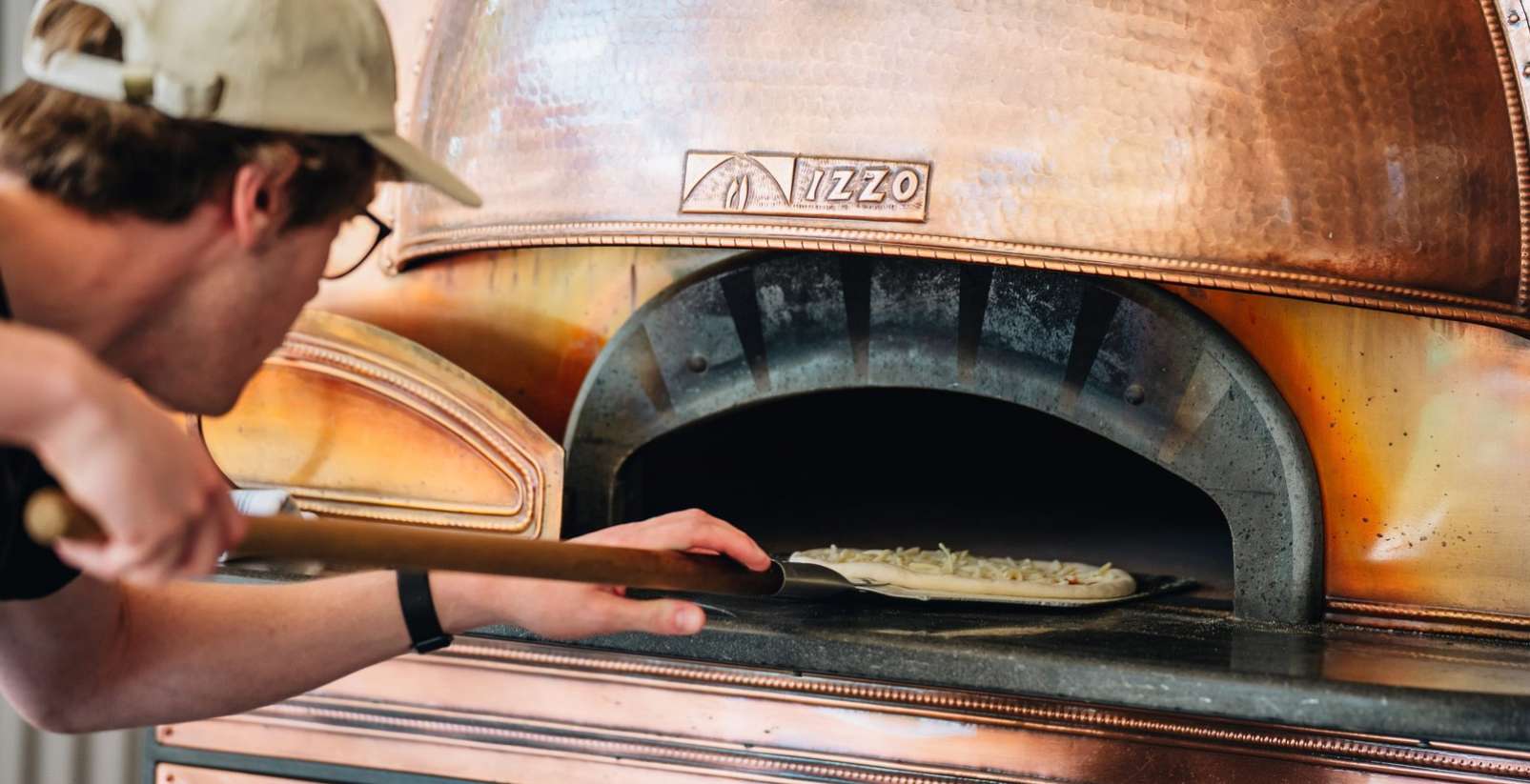 man putting pizza into woodfire stone oven